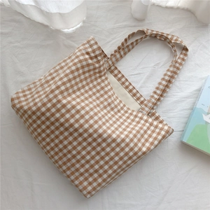 Flat lay view of a brown and white checkered cotton tote bag on a soft fabric surface