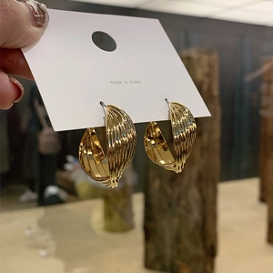 Macro detail of gold layered textured C-hoop earrings featuring woven metallic lines