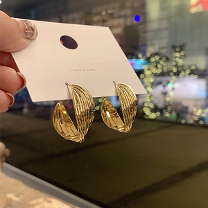 Detail of gold twisted C-shape earrings with metallic gloss on a white card display