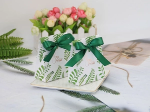 Detail of forest style wedding gift box with green leaf pattern and ribbon on porcelain plate