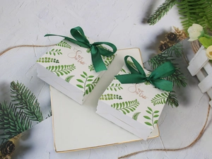 Close-up of European gift boxes with green leaf patterns and satin ribbons on a white plate