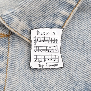 Détail de la broche émaillée partition avec texte 'Music is my Escape' sur jean