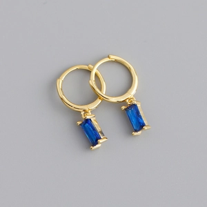Détail de boucles d'oreilles huggie dorées avec pendentifs rectangulaires en gemme bleue