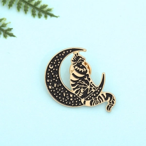 Close-up of a black enamel cat pin resting on a crescent moon with starry details