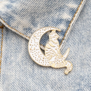 Macro view of a cute enamel cat sitting on a moon brooch pinned on denim jacket