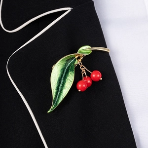 Close-up of a red cherry brooch with green leaves pinned on a black suit lapel