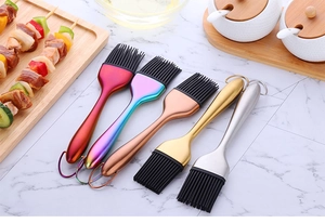 Cinque pennelli in silicone con manici metallici su un piano da cucina in marmo bianco