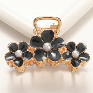 Detail of gold metal hair claw clip featuring black enamel flowers and white pearls