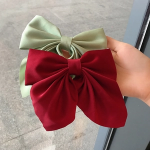 Elegant satin bow hair clips in wine red and sage green shown in hand for size