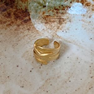 Detail of a minimalist gold braided multi-layer wrap ring on a rustic ceramic bowl