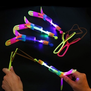 Close-up of hands launching glowing LED slingshot arrow toy against a dark background