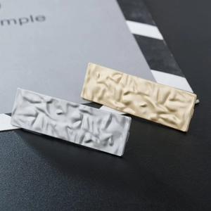 Close-up of matte gold and silver alloy hair clips with unique pleated metal texture