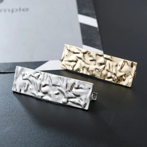 Detail of gold and silver rectangular metal hair clips with hammered texture on dark surface
