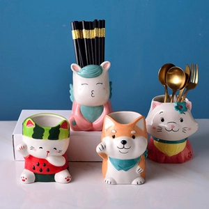 Detalle de cuatro porta utensilios de cerámica con diseños de unicornio y gato en mesa blanca