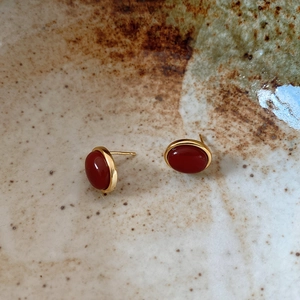 Macro shot of retro oval red agate stud earrings with gold bezel on rustic pottery