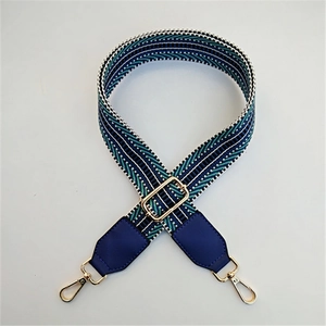 Detail of adjustable PU leather wide bag strap with blue geometric jacquard pattern and gold clips