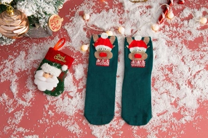 Close-up of green knitted Christmas socks with 3D reindeer decor and festive background