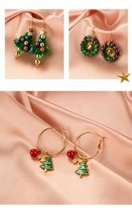 Three pairs of festive Christmas earrings including trees and wreaths on pink silk cloth