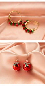 Close-up of festive Christmas bell hoops and red berry drop earrings on pink silk