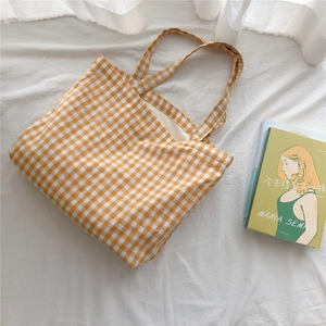 Detail of yellow gingham cotton tote bag lying on soft white fabric with a book