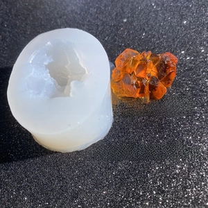 Macro detail of translucent silicone mold and orange resin crystal cluster on black glitter