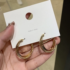 Close-up of golden layered hoop earrings with twisted metallic lines held by hand