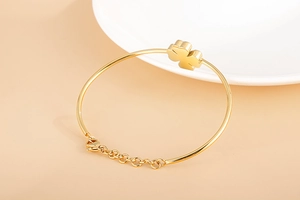 Detailed side view of a gold four-leaf clover bangle with adjustable lobster clasp chain