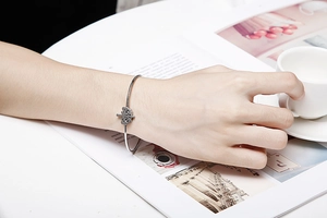 Gros plan d'un bracelet ouvert en argent avec arbre de vie sur un bureau blanc