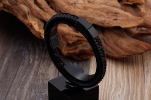 Détail macro d'un bracelet en cuir tressé noir avec fermoir mat et touches de surpiqûres rouges