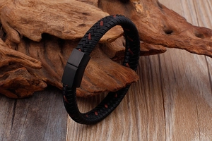 Vue macro d'un bracelet en cuir tressé noir avec coutures rouges et fermoir en métal