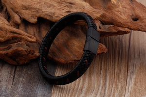 Détail du bracelet en cuir tressé noir avec couture rouge et fermoir magnétique mat