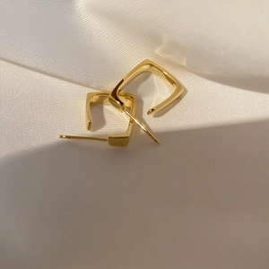 Minimalist square golden geometric hoop earrings with polished metal finish on silk background