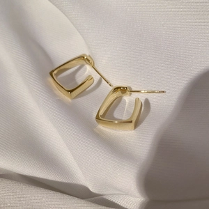Detail shot of golden geometric square C-shaped earrings on elegant white silk background
