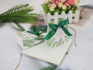 Detail of paper wedding favor box with leaf pattern and green ribbon on porcelain plate