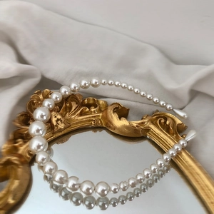 Elegant pearl headband with gradient beads on gold frame against white fabric background