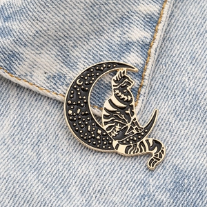 Detail of a black and gold enamel cat pin on a crescent moon over blue denim fabric