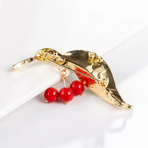 Back view of stylish cherry fruit brooch with gold leaves and red beads on white backdrop
