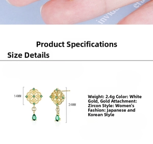 Detail of vintage gold earrings with emerald green teardrop zircon and hollow patterns