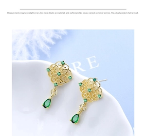 Detailed macro view of vintage gold hollow carved earrings with emerald green teardrop gems