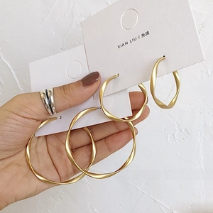 Detail view of twisted matte gold geometric hoop earrings held by hand for size contrast