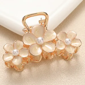 Macro shot of gold alloy hair claw with three cream enamel flowers and white pearls
