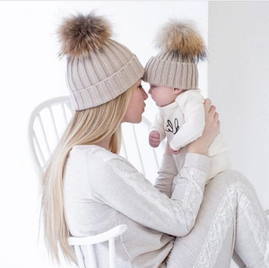 Beigefarbene Strickmützen für Mutter und Baby mit großen Pelzbommeln für warme Wintertage
