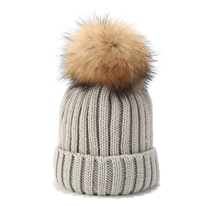Detalle del tejido de punto y del pompón de pelo suave en el gorro gris claro de invierno