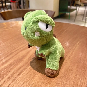 Cute green plush dinosaur keychain featuring sleepy eyes on a wooden cafe tabletop