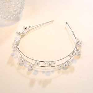 Close-up of double-layer silver headband with assorted sizes of white pearls on beige surface