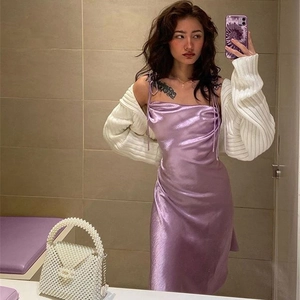 Détail d'une robe en satin violette associée à un gilet en maille blanche devant un miroir