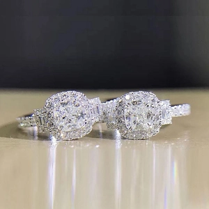 Macro shot of two silver halo rings with cushion cut stones on a reflective surface
