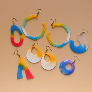 Macro detail of geometric resin earrings with colorful gradient patterns and metal hooks