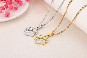 Detail of silver and gold plated paw print necklaces with sparkling crystals on a beige surface