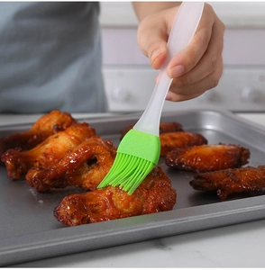 Close-up of a green silicone brush applying sauce to chicken wings on a baking tray